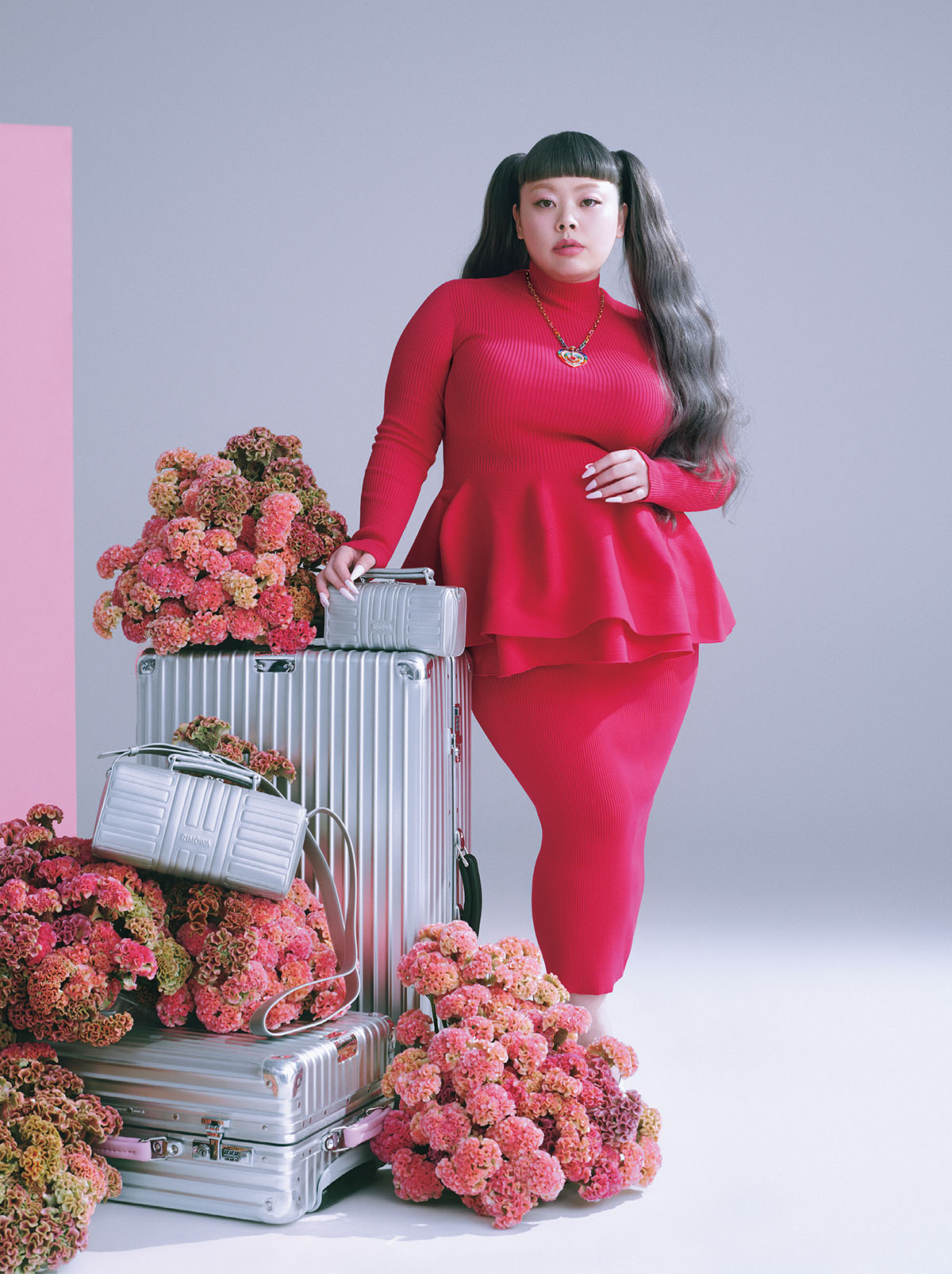 <バッグ上から>右手『Groove』クロスボディバッグ スモール(W19.5×H10×D8.5cm/取り外し可能なストラップ付き)¥180,400 『Classic』チェックイン L(ブラックレザーハンドル&ホイール/W53×H79×D28cm/6kg・84L)¥292,600 『Groove』クロスボディバッグ ラージ(W28×H13×D10cm)¥266,200 カスタム仕様のアルミのスーツケース『Classic』キャビン(W40×H55×D23cm/4.3kg・36L)¥237,600 ピンクレザーハンドル¥46,200 ピンクホイール¥24,200/すべてRimowa(リモワ クライアントサービス)トップ¥49,500 スカート¥59,400/ともにCFCL(シーエフシーエル)ネックレス(PG×YG×WG×カラーストーン×ハードストーン×ダイヤモンド)¥26,202,000/Fred(フレッド カスタマーサービス)