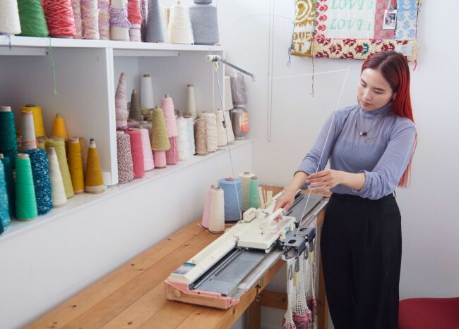 立って押し引きしながら編みのが倉谷さん流。色を選んで変える作業が多いため、立ったままの方が集中できるのだとか。