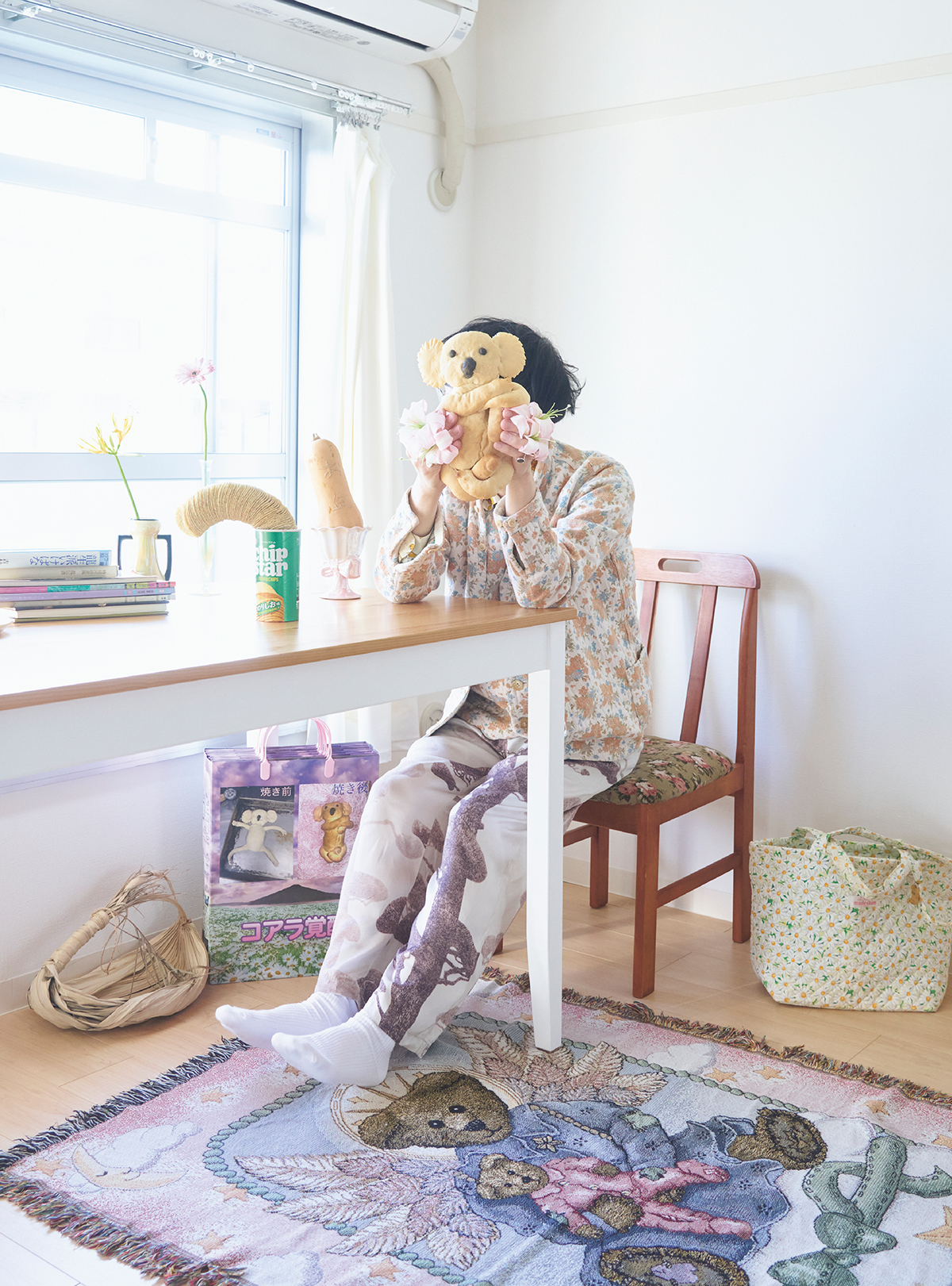 団地の一画に構えたアトリエにて撮影（顔出しNG）。団地好きが高じて入居した光差す一室。手にした自家製コアラパンは2024年、コアラ上陸40周年に寄せて展示。オリジナル紙袋（左下）も制作した。「小麦は植物、つまりいけばなです。食べてもおいしい！」Portrait : Ayako Masunaga