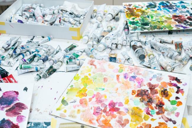 作業机一面にひろがる絵の具の数々。「パレットに色をたくさん置く状態そのものが好きなんです。色があればあるほど安心します」。既存の絵の具の色からインスピレーションが湧くこともある