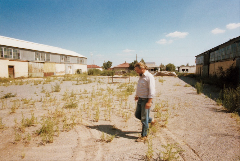 ドナルド・ジャッド、マンサナ・デ・チナティの中庭にて、自作『デイヴ・シャックマンに』（1964年）と共に　1975年撮影　Photo Jamie Dearing © Judd Foundation. Jamie Dearing Papers, Judd Foundation Archives, Marfa, Texas.  Donald Judd Art © 2026 Judd Foundation/ARS, NY/JASPAR, Tokyo.